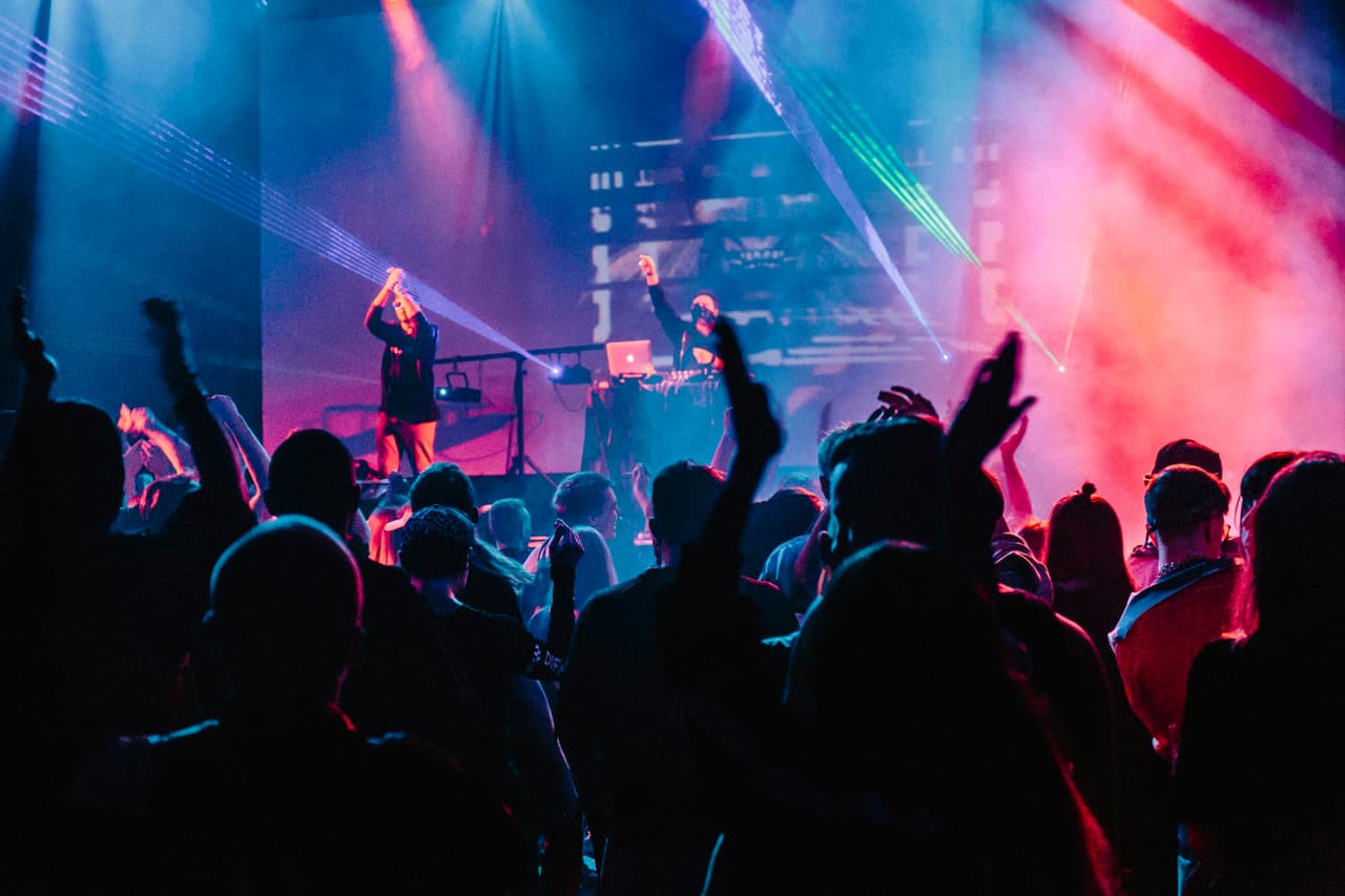 Feestpubliek met handen in de lucht onder paarse lichtshow tijdens een DJ-optreden
